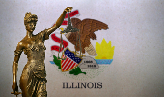 Bronze statue of Lady Justice holding a scale and sword standing in front of the Illinois flag